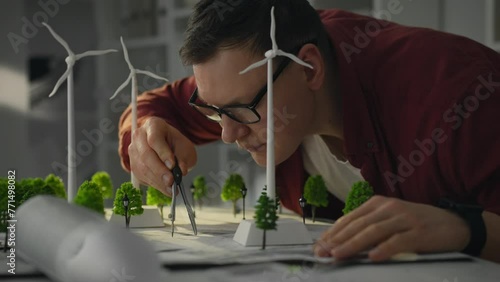 In modern office white male engineer is hard at work researching green energy using models of wind turbines. His work is aimed at creating a concept for future city based on alternative energy sources photo