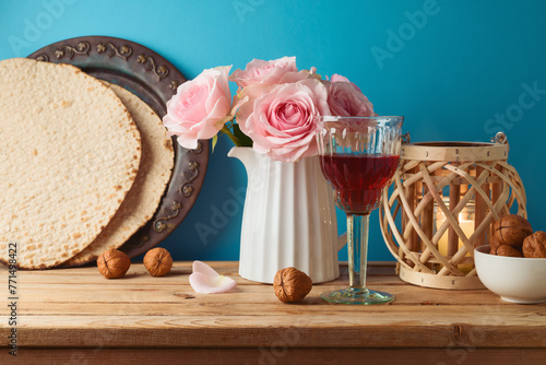 Jewish holiday Passover concept with wine glass, matzah and flowers on wooden table over blue background.