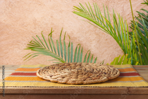Empty wooden table with wicker place mat over wall with palm tree background. Summer picnic mock up for design and product display.