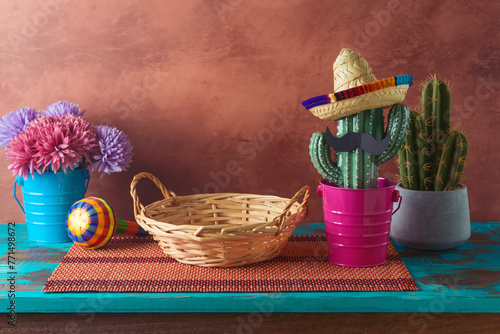 Empty wicker basket on wooden blue table with cactus decoration over wall  background. Mexican party mock up for design and product display