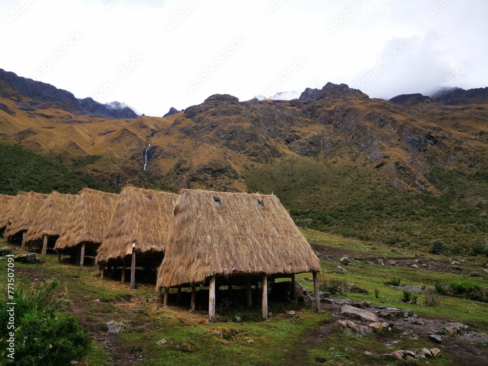 many thatched houses in the field with mountains behind them many thatched houses in the field with mountains behind them