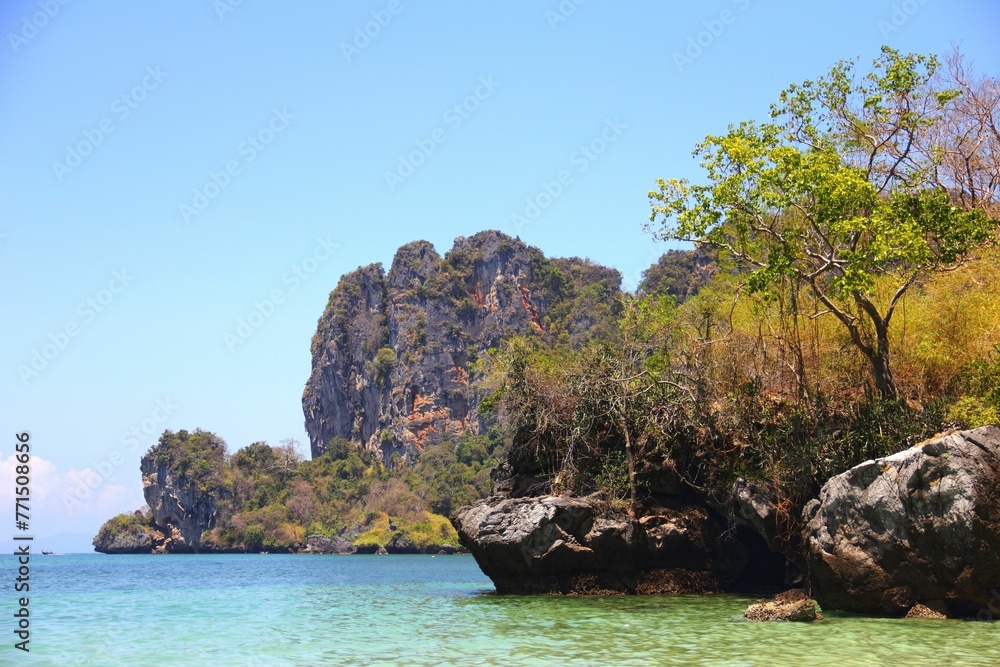 Obraz premium Tranquil sea with a rocky shoreline and lush vegetation. Railay Beach, Thailand.