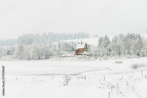 a rural scene with some trees and an old house on the bank of a frozen
