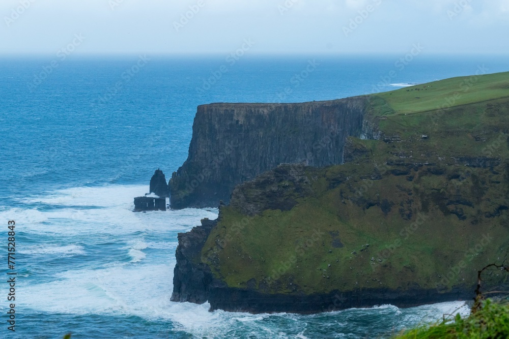 Lush, green grassy field with gentle waves lapping against the cliffs on a cloudy day