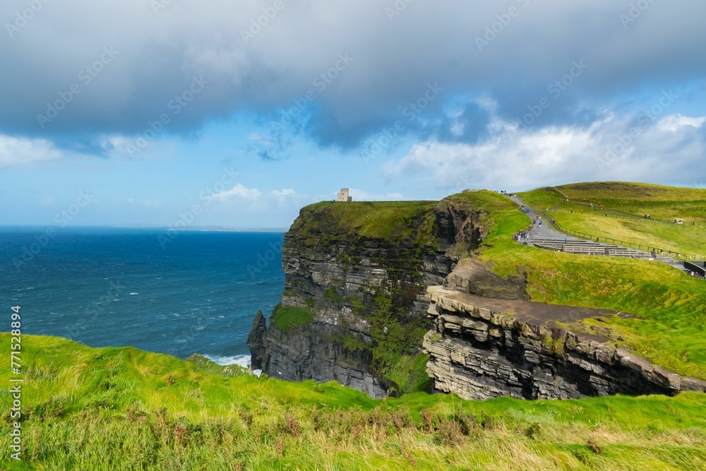 Lush, green grassy field with gentle waves lapping against the cliffs on a cloudy day