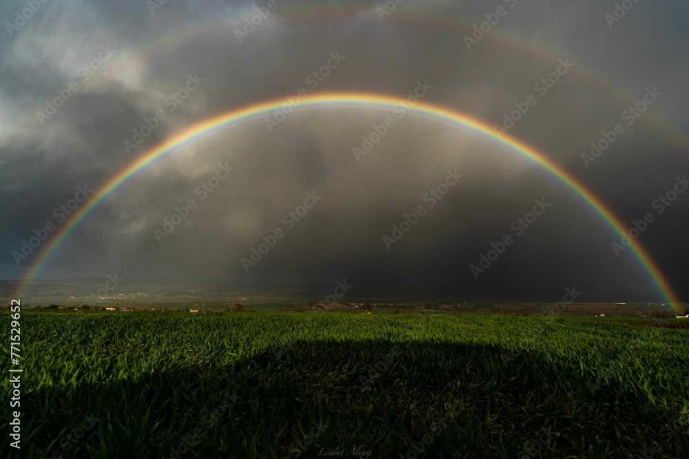two rainbows with clouds in the background, on grass field two rainbows with clouds in the background, on grass field