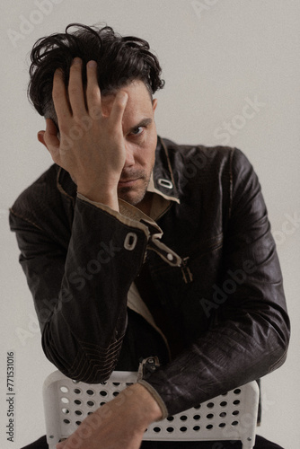 a man in a leather jacket covers half his face with his hand