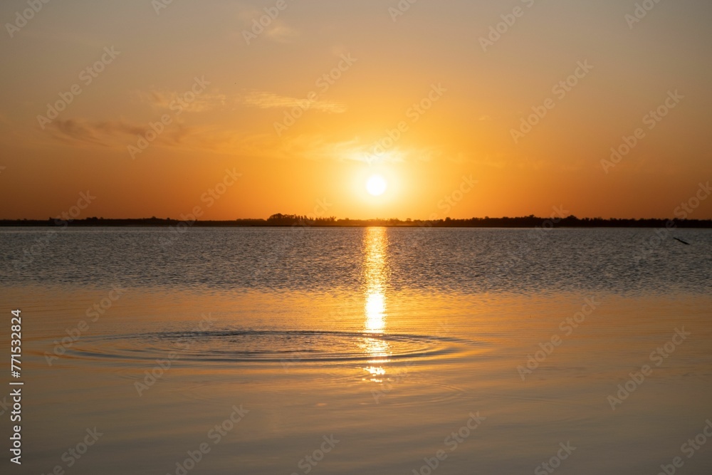 Vibrant orange sunset reflected on the calm water surface Vibrant orange sunset reflected on the calm water surface