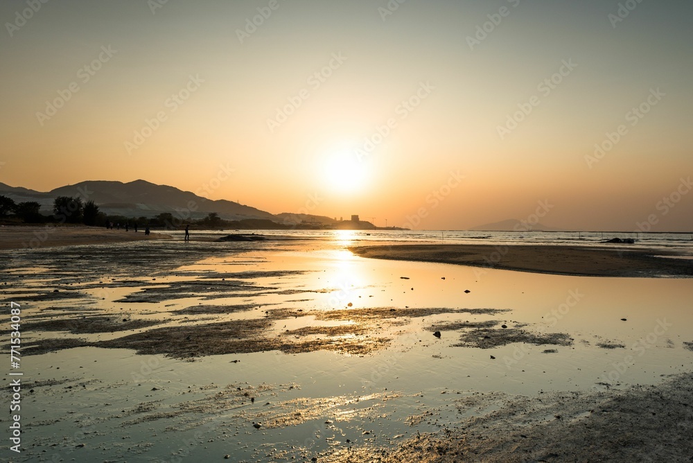 Tranquil beach landscape featuring wet sand leading to the horizon, with majestic mountains