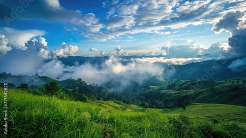Green grass field on slope with blue sky and clouds background, cloud mountain tropic valley landscape, wide misty panorama