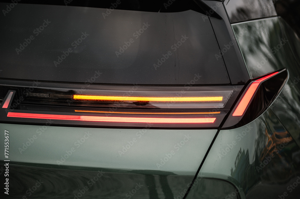Obraz premium Right turn indicator signal. Red tail lights closeup. Modern concept supercar exterior design detail, headlight. Back view. Right rear light shining on new modern electric sedan car. Concept of future