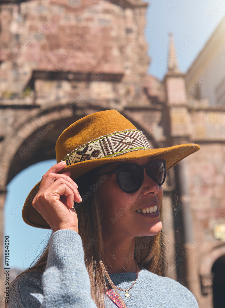 Stepping Into Another World. Historical Tourism Concept. Young woman traveler in brown hat walks through of the Santa Clara Arch in San Francisco square. Cusco, Peru.
