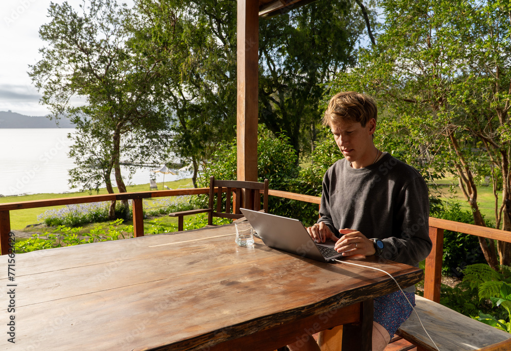 Man working remotely online from his vacation home, dressed in swimwear, enjoying the outdoors. Digital nomad
