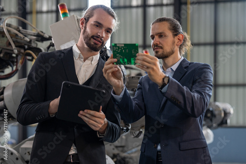 Two professionals in suits engaged in a discussion and held circuit board for production of robot arm welding machines in industrial robots in a technology facility.