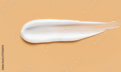 Top view of white cosmetic smear closeup on beige background. Skincare spa product sample or makeup swatch with creamy texture macro. Cream smudge drop, moisturizer, balm, gel, lotion sample