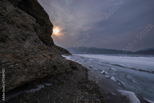 icy mountain lake with rocks, snow and hummocks in early spring in gloomy weather, Bartogay reservoir in Kazakhstan. photo