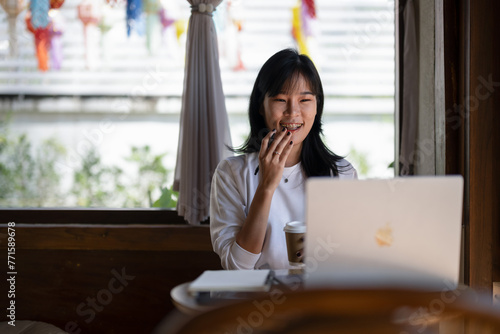 .Young Asian woman enjoying coffee while having a pleasant video call on a laptop in a coffee shop.