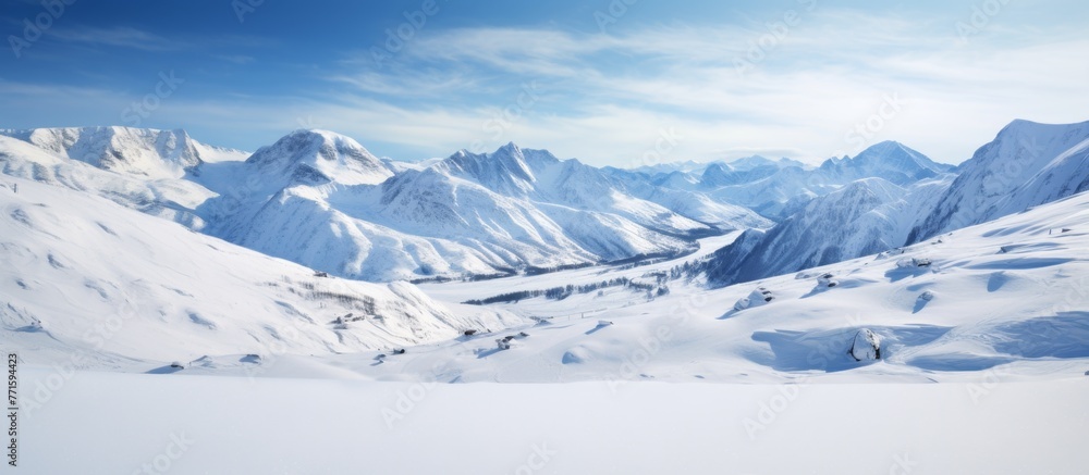 Obraz premium A picturesque natural landscape of a snowy mountain range under a blue sky with scattered clouds. The ice caps glisten on the slopes as the wind blows across the horizon