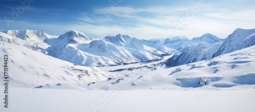 A picturesque natural landscape of a snowy mountain range under a blue sky with scattered clouds. The ice caps glisten on the slopes as the wind blows across the horizon