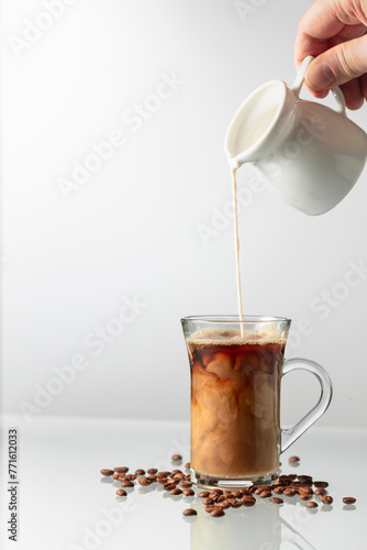 A man's hand pours cream into a glass of coffee.