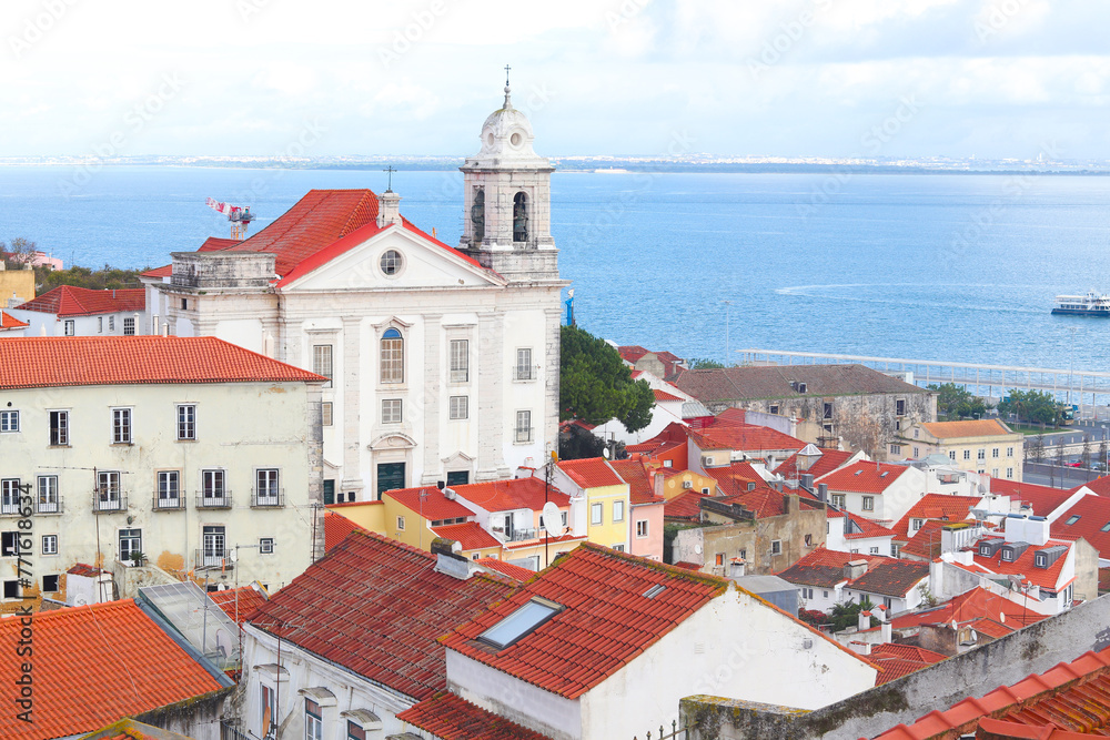 Fototapeta premium View of historical houses with red roofs, Lisbon, Portugal. Amalfa district. The Miradouro de Santa Luzia viewpoint. The Church of Sao Vicente of Fora in the background.