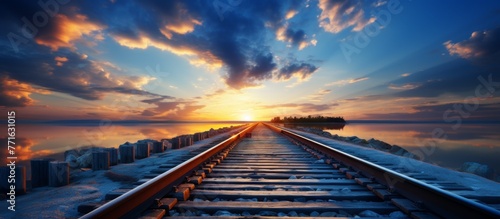 A train track stretches towards the electric blue ocean as the sun sets, creating a symphony of colors in the sky with fluffy cumulus clouds