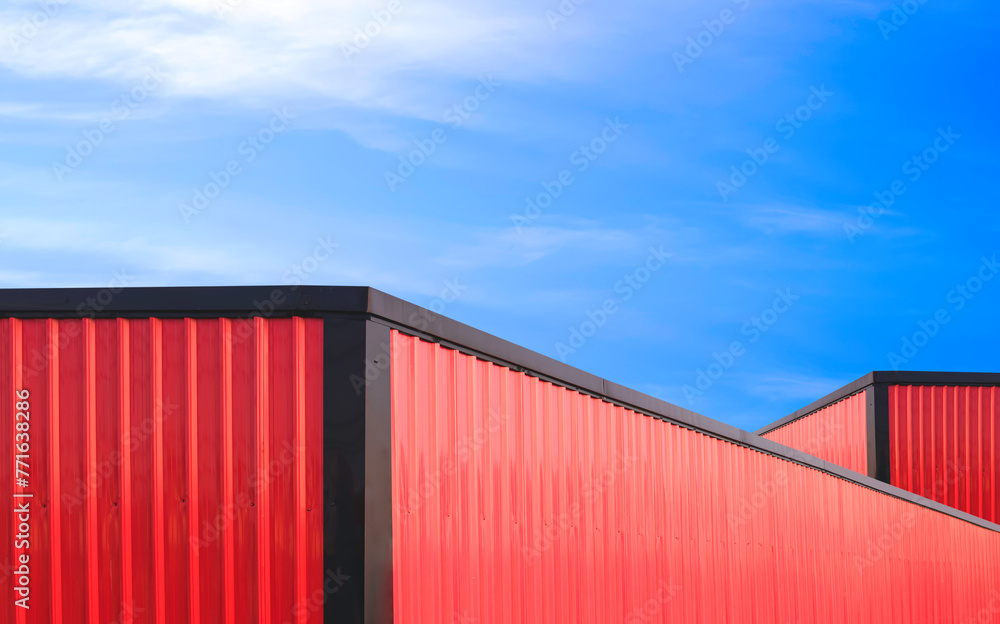 Red and black aluminium roofs of two metal industrial warehouse buildings against blue sky background in perspective side view and minimal style Red and black aluminium roofs of two metal industrial warehouse buildings against blue sky background in perspective side view and minimal style