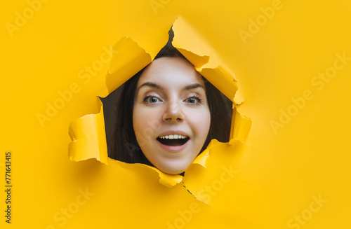 A laughing dildo girl looks out from a torn hole in yellow paper and smiles cheerfully. The concept of espionage or eavesdropping. Sales discounts. Copy space. © shchus
