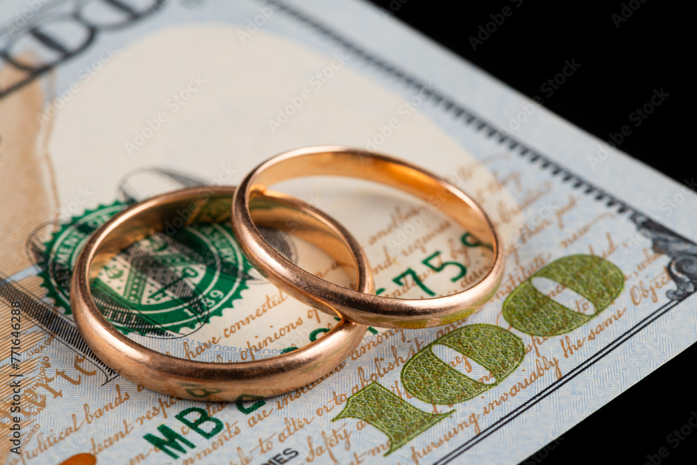 Gold wedding rings against the background of a fragment of a 100 US dollar bill Gold wedding rings against the background of a fragment of a 100 US dollar bill