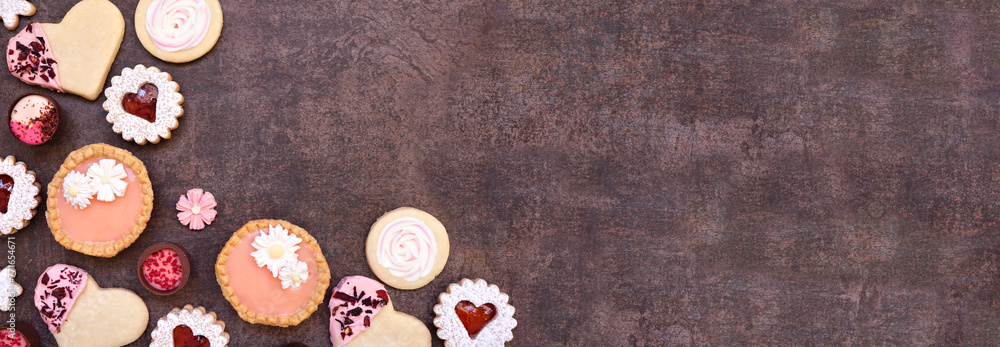 Fototapeta premium Mothers Day or love themed baking corner border with assorted cookies and sweet treats. Above view on a dark stone banner background with copy space.