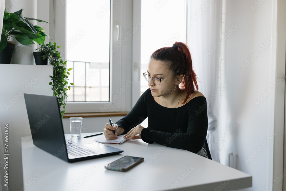 Young female student using laptop and notebook, studying at home Young female student using laptop and notebook, studying at home