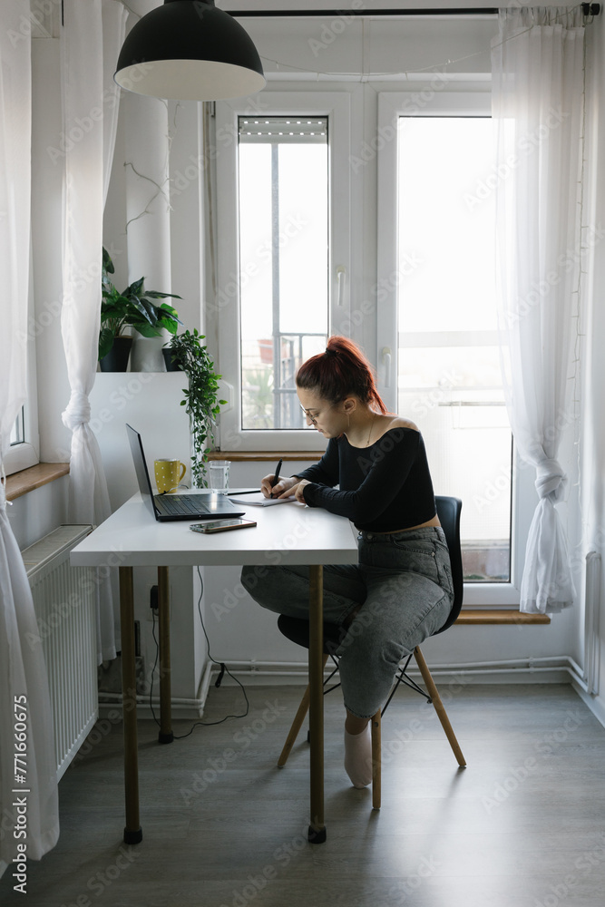 Young female student using laptop and notebook, studying at home Young female student using laptop and notebook, studying at home