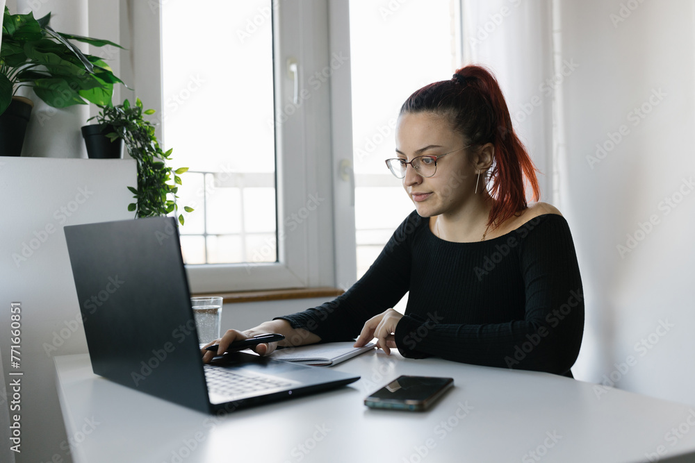 Young female student using laptop and notebook, studying at home Young female student using laptop and notebook, studying at home