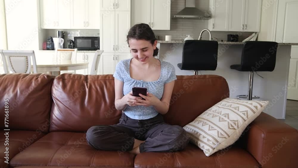 Teenage Girl Texting on Smartphone at Home. A young girl sits comfortably on a brown leather couch, deeply engaged with her smartphone. Teenage Girl Texting on Smartphone at Home. A young girl sits comfortably on a brown leather couch, deeply engaged with her smartphone.