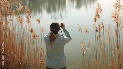 Woman explorer with binoculars watching birds and animals at lake. Ornithology. Handheld video photo