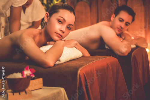 Caucasian couple customer enjoying relaxing anti-stress spa massage and pampering with beauty skin recreation leisure in warm candle lighting ambient salon spa at luxury resort or hotel. Quiescent