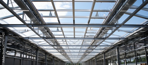 Admiring the symmetry of the metal beams in the composite material roof, with tints and shades, from the clear glass ceiling of the building