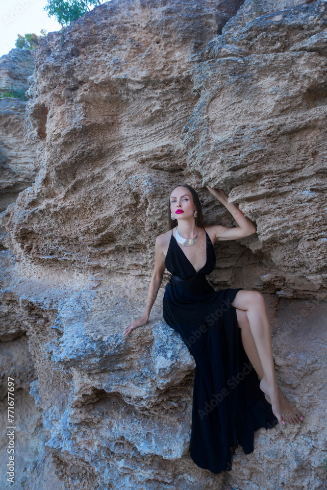 woman in black dress stands looking into the sea on a rock woman in black dress stands looking into the sea on a rock
