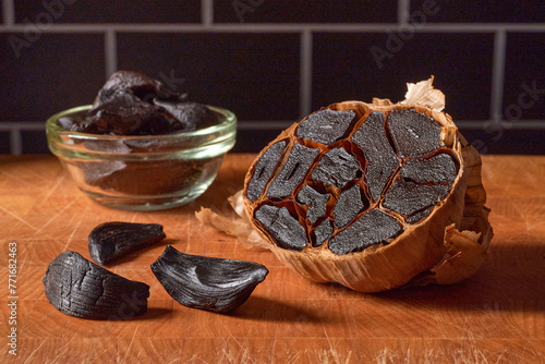 Black garlic on cutting board, dark background
