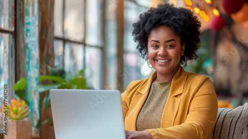 Smiling plus-size woman in a yellow blazer working on a laptop in a cafe