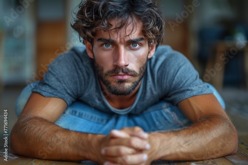 High-definition portrait featuring a man with intense gaze and stubble, in a casual grey shirt, leaning forward with folded arms © Larisa AI