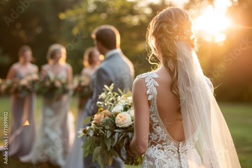 The image captures a stunning back view of a bride holding a bouquet at a sunset wedding ceremony with bridal party photo