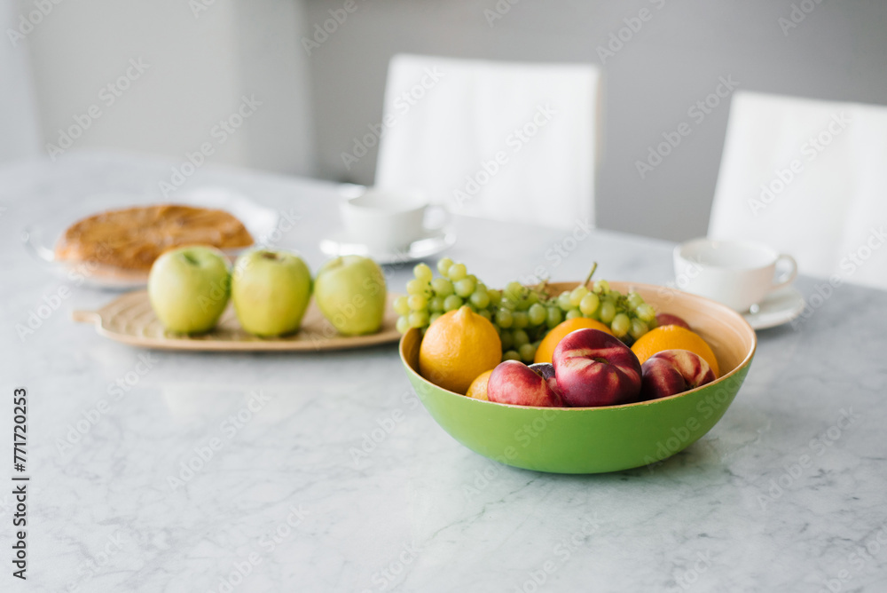 Fresh fruit, peaches, grapes and oranges, apple in a plate on the marble table in the kitchen. Healthy and wholesome food Fresh fruit, peaches, grapes and oranges, apple in a plate on the marble table in the kitchen. Healthy and wholesome food