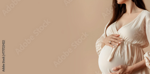 A pregnant woman gently holds her belly on a brown background