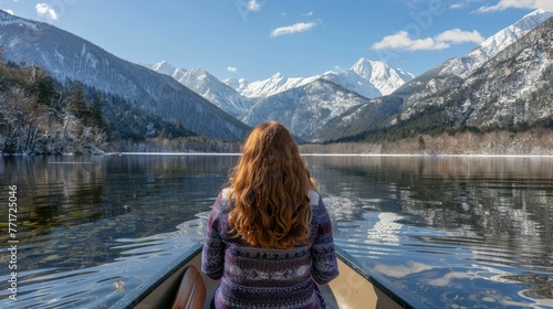  A woman sits on a boat amidst a tranquil lake, with towering mountains and snow-capped peaks visible in the distance