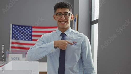 Smiling young man pointing to 'i voted' sticker with american flag in polling station photo