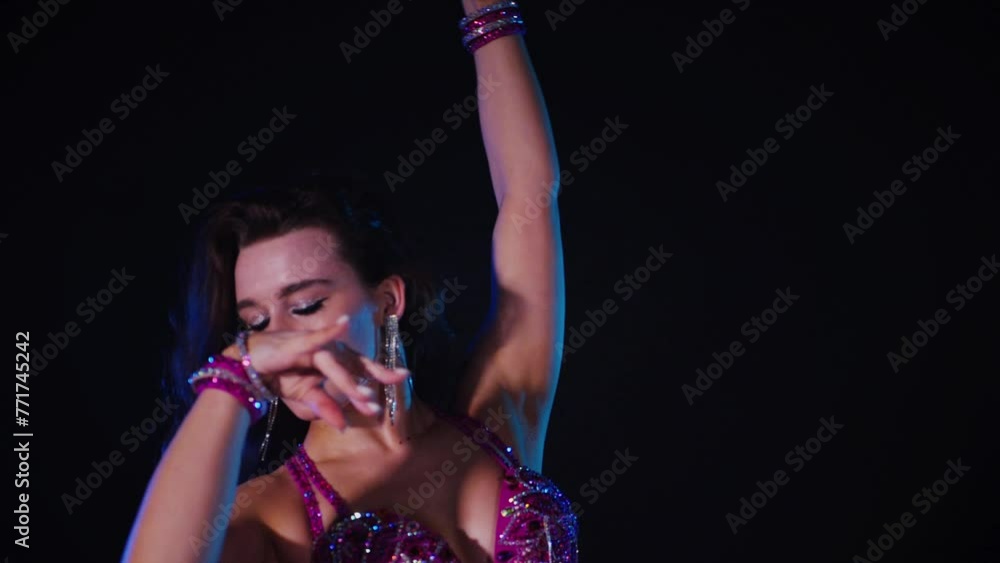 Woman in purple dress gracefully dancing belly dance in dimly lit room. Slow motion shooting. Elegantly dressed woman moving to music and dancing oriental dances in dark setting. Female dancer wearing Woman in purple dress gracefully dancing belly dance in dimly lit room. Slow motion shooting. Elegantly dressed woman moving to music and dancing oriental dances in dark setting. Female dancer wearing