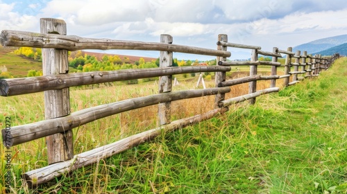  Wooden fence separates lush green field from majestic mountain range in background