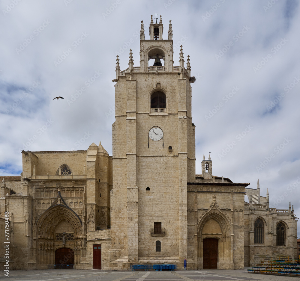 Fachada con dos puertas y torre con campana y  reloj de la Catedral de San Antolín de Palencia sede episcopal de la ciudad de Palencia, sobre cielo en colores grises al atardecer