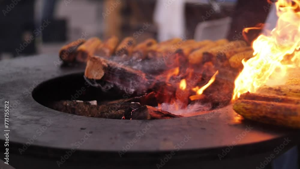 Burnt golden corncobs are cooked with smoke and flame on a grill or barbecue. Close-up of corn vegetables being cooked on a round metal grill. Picnic or party in the countryside. Summer weekend with h